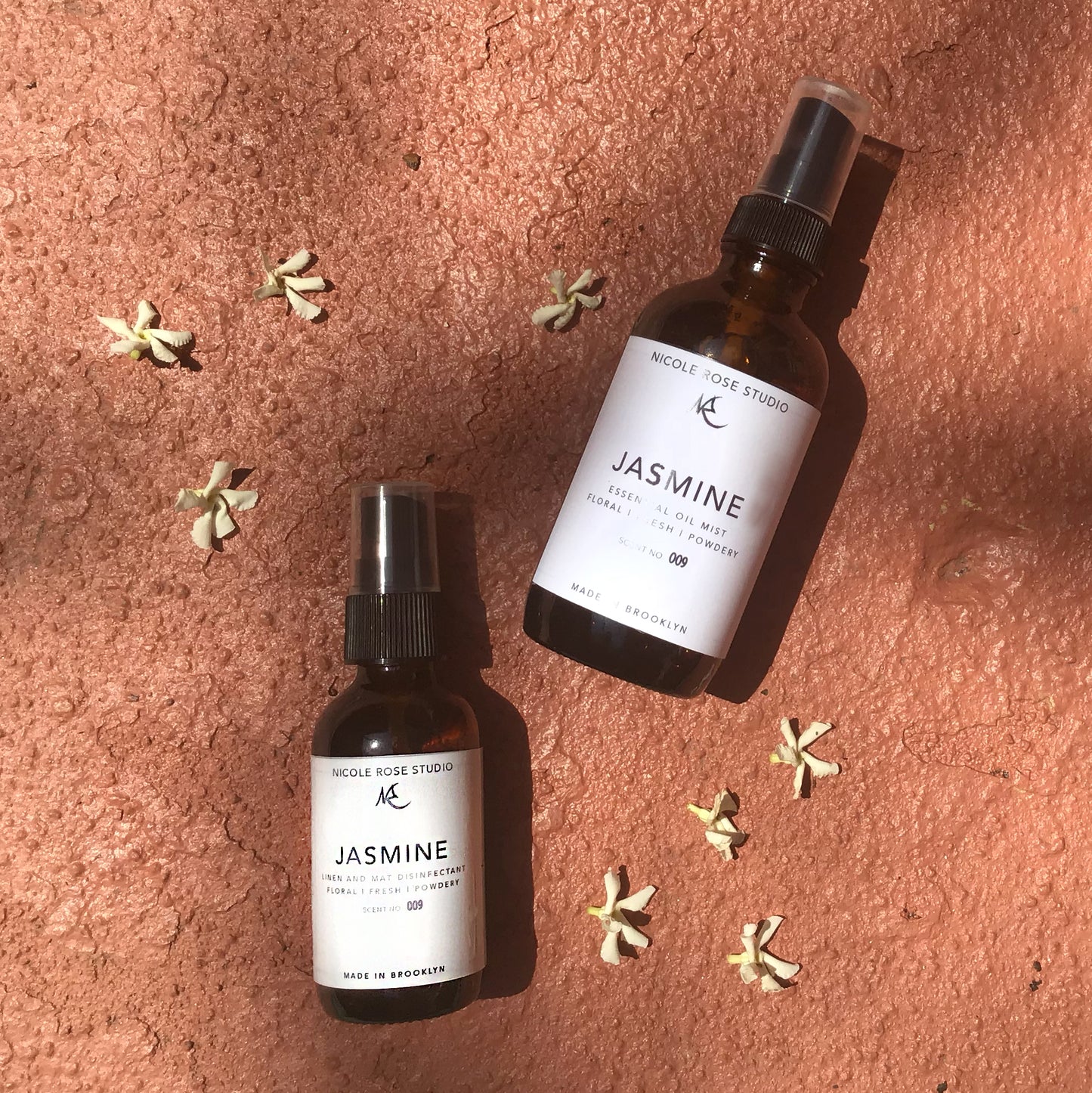 Two bottles of Nicole Rose Studio Jasmine product on a textured surface with scattered flowers.Best online retail store. Axis-Dynamics