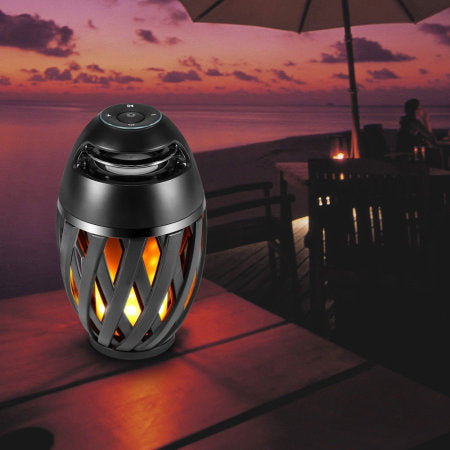 Black lattice-patterned lantern with flame effect on a table at sunset.