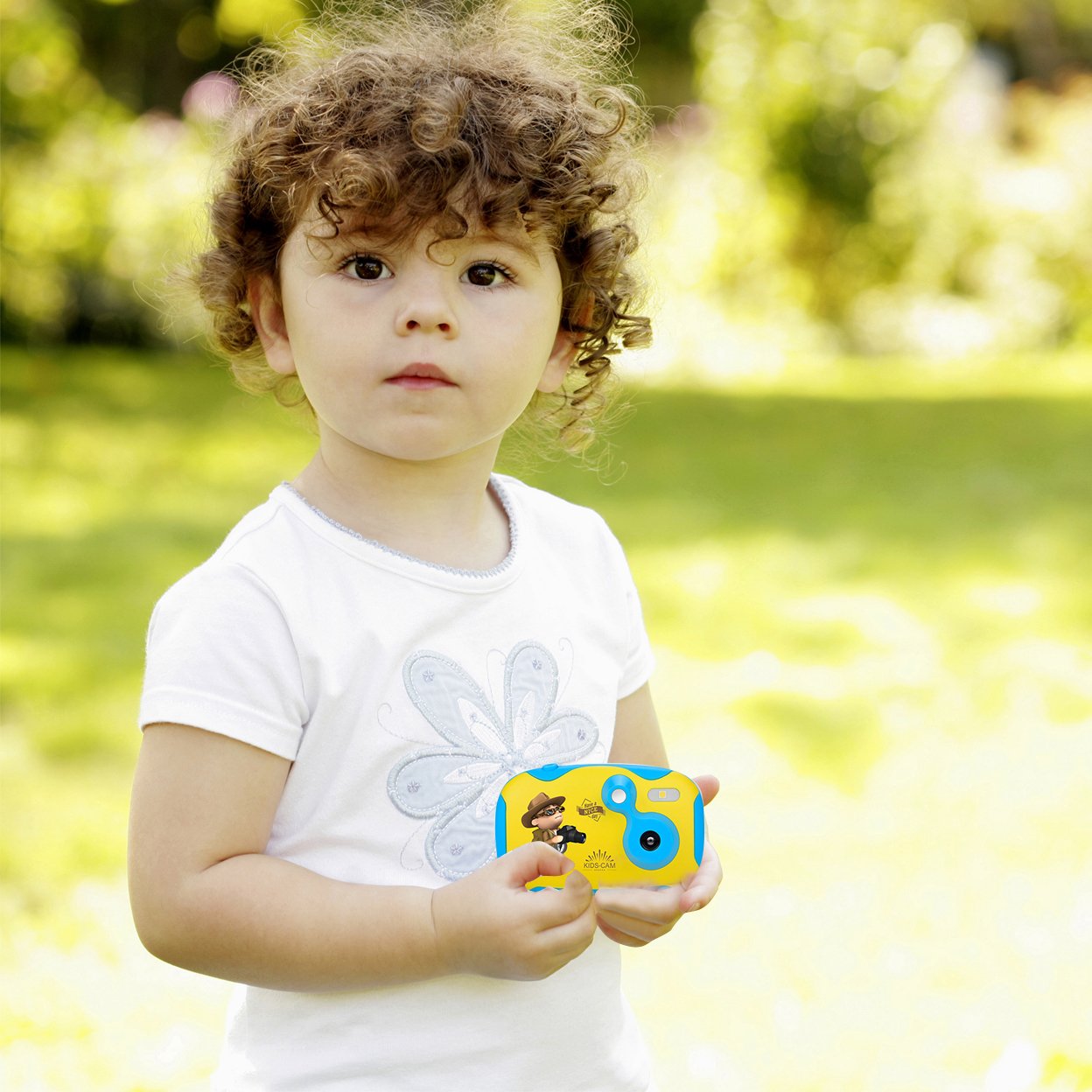 Child holding a toy camera outdoors with a blurred green background