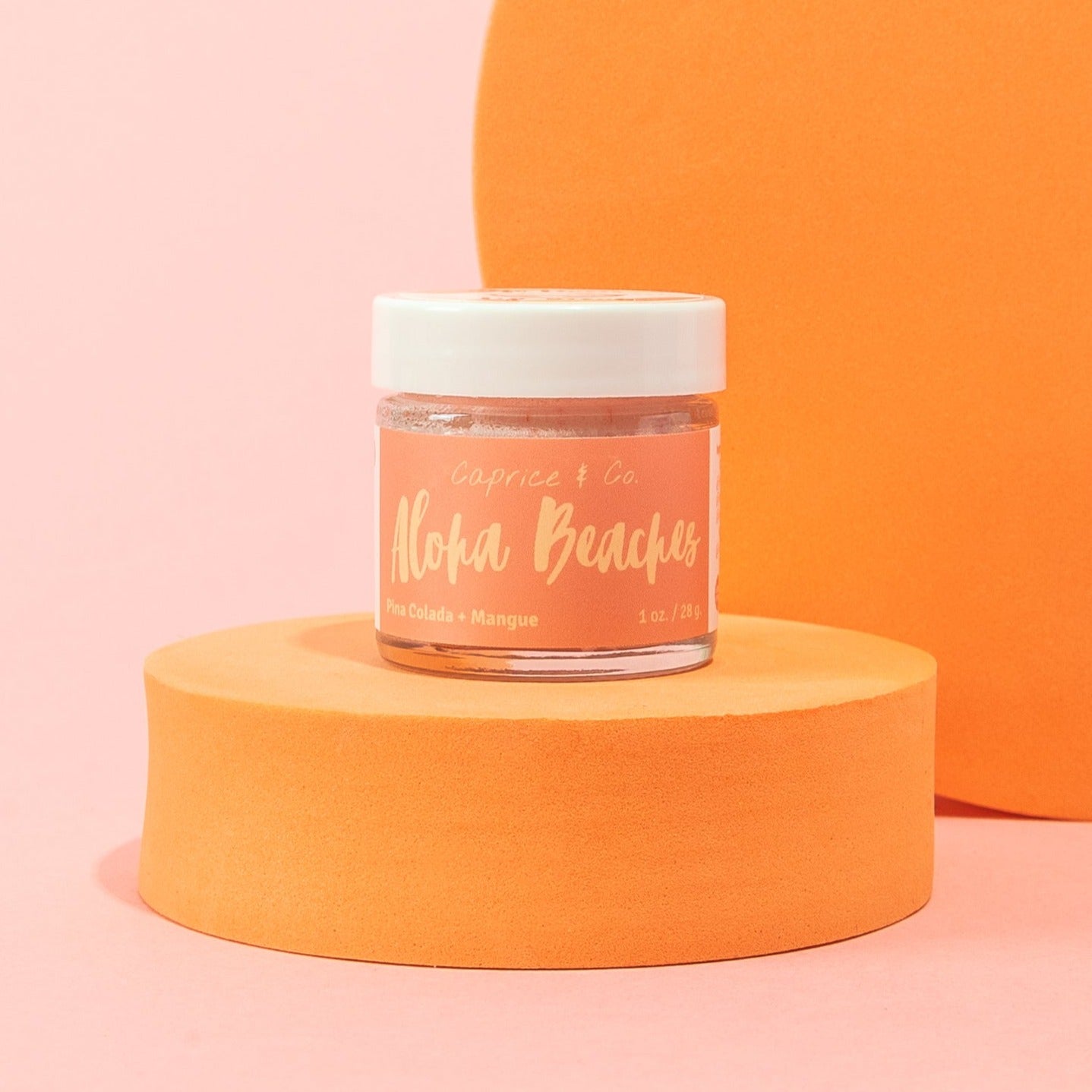 A small clear jar of Caprice & Co. 'Aloha Beaches' nail powder sits on a round orange pedestal against a pink and orange studio background. Best online retail store. Axis-Dynamics