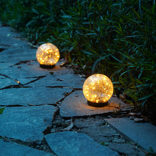 Two glowing spherical lights on a stone pathway with greenery in the background