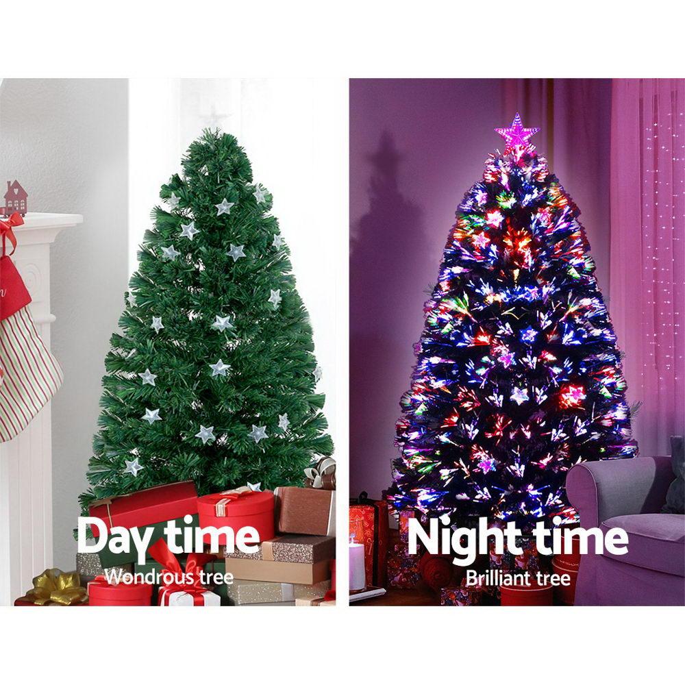 A side-by-side comparison showing a green artificial Christmas tree in two settings: 'Day time' with white star ornaments and wrapped gifts, and 'Night time' illuminated with multicolored lights and a pink star topper.