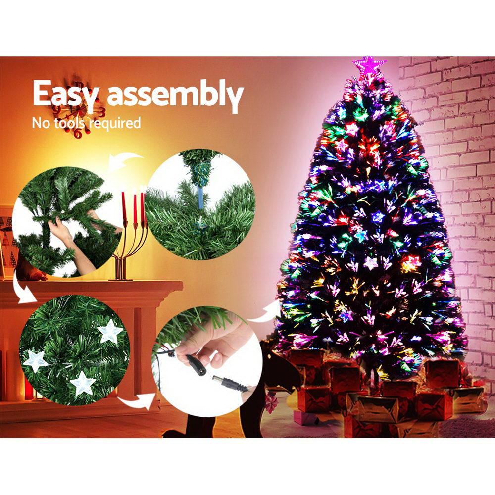 A lit multicolor Christmas tree stands against a brick wall with wrapped presents underneath. The left side includes promotional text reading 'Easy assembly' and circular inset close-ups showing parts of the tree and assembly details. Axis-Dynamics online retail store