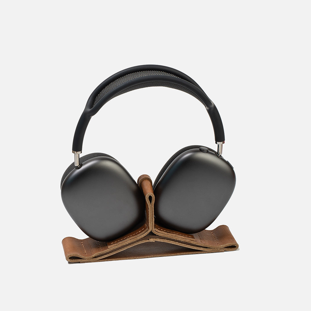 Black headphones on a brown leather stand against a white background