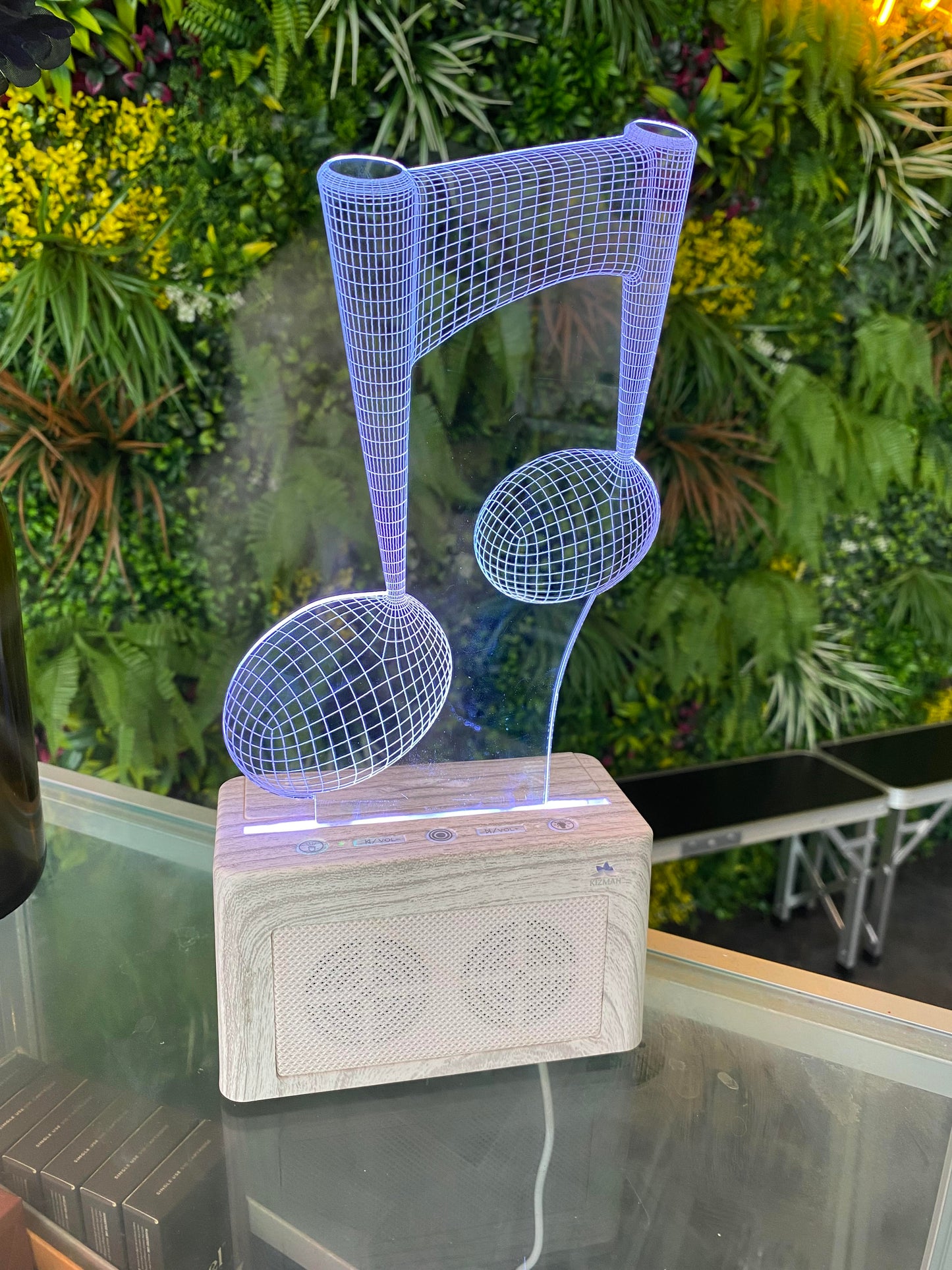 3D wireframe sculpture of a music note on a wooden base with a blurred green plant background