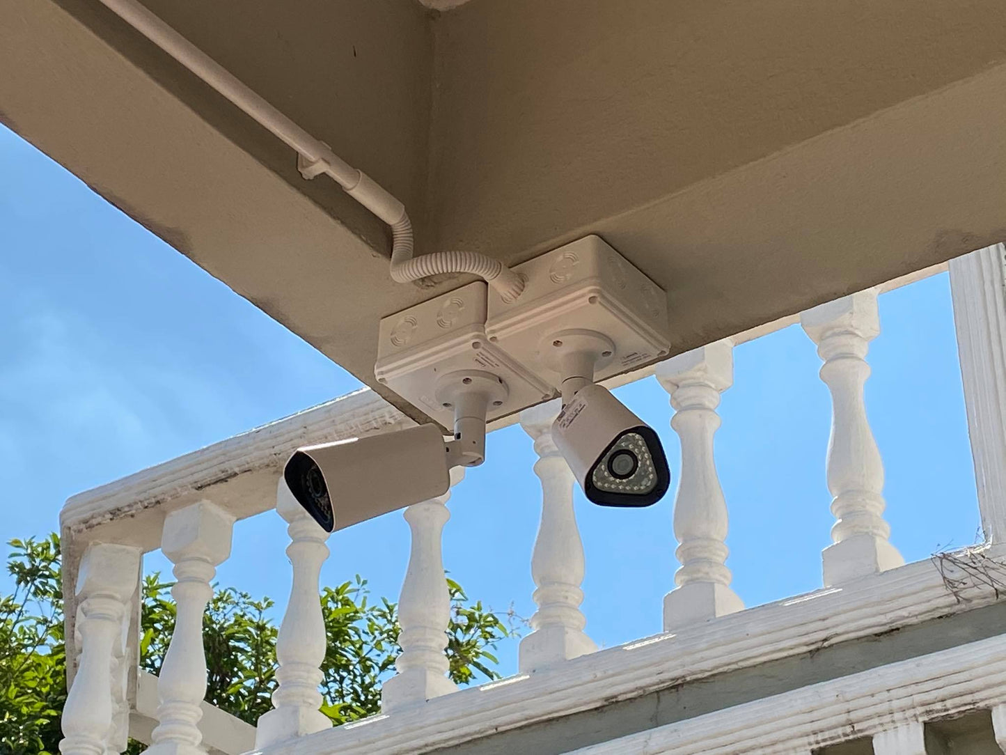 Security cameras mounted on a balcony railing with a clear blue sky background.