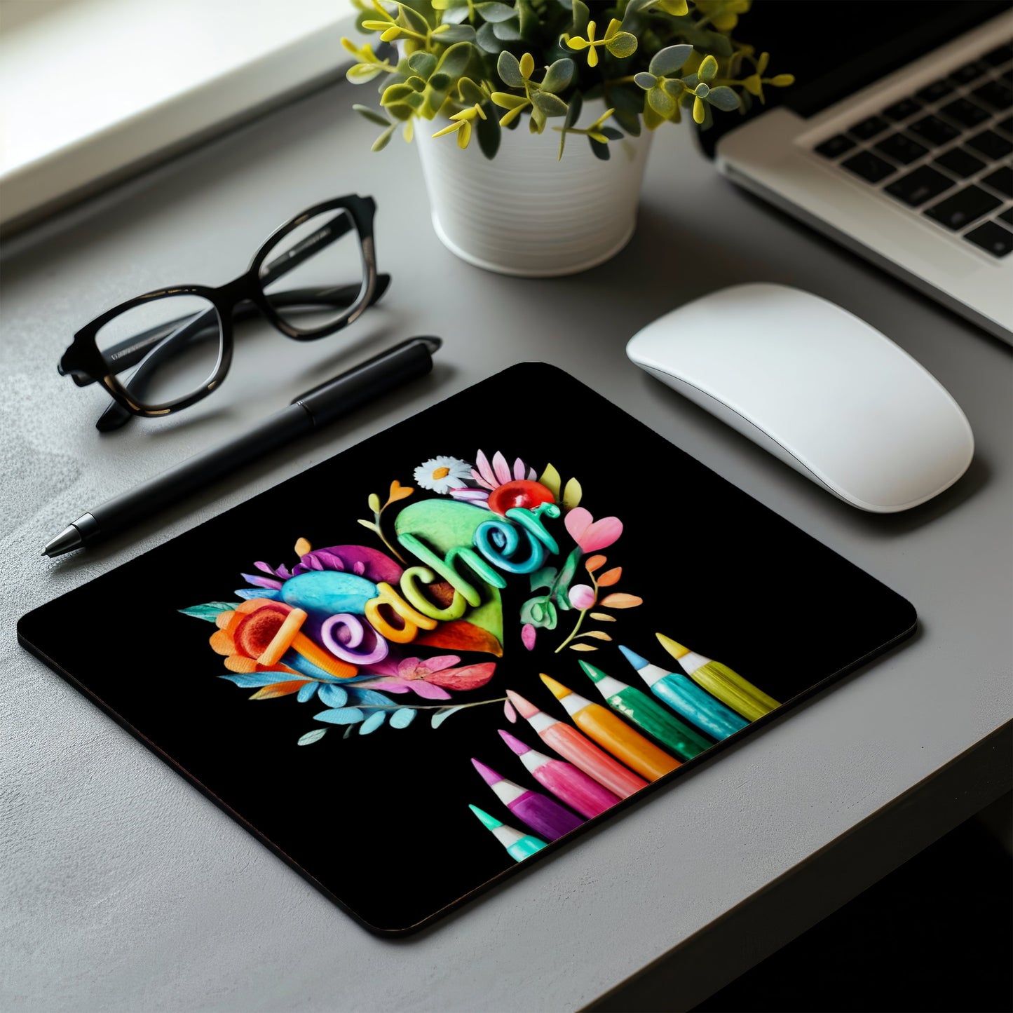 Colorful 'I love to teach' mouse pad on a desk with a laptop, glasses, pen, and mouse. 