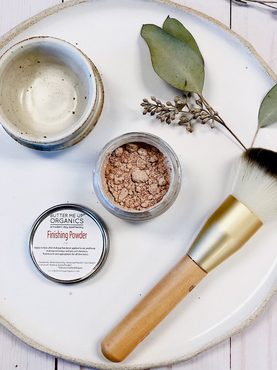 Cosmetic products including a container of finishing powder, a brush, and a small dish on a white surface. deep hydrating body butter for winter dry skin and online store. Axis-Dynamics