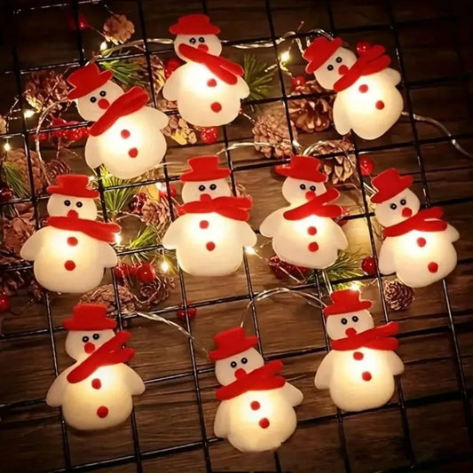 String of snowman-shaped lights on a wooden surface with Christmas decorations.