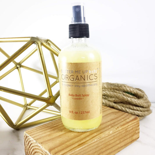 Bottle of Terme Up Organics Baby Butt Spray on a wooden block with geometric gold sculpture and rope in the background.