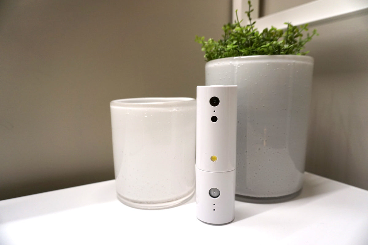 White electronic device on a surface with two white containers and a plant in the background