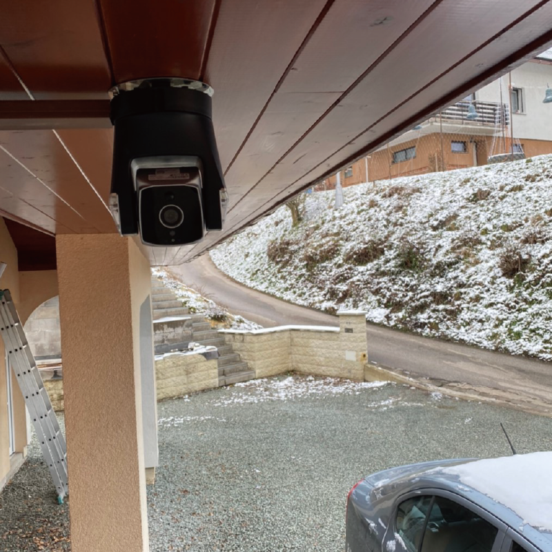 Security camera mounted on a house exterior with a snowy landscape in the background.