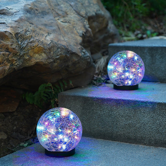 Two colorful LED globe lights on stone steps with rocks and greenery in the background