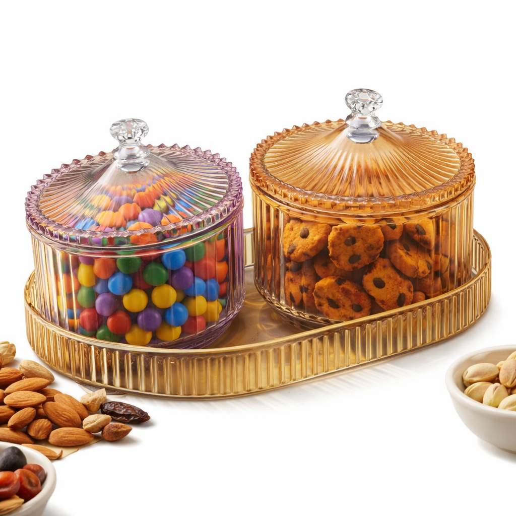 Two glass candy jars with lids on a gold tray, filled with colorful candies and cookies, on a white background.