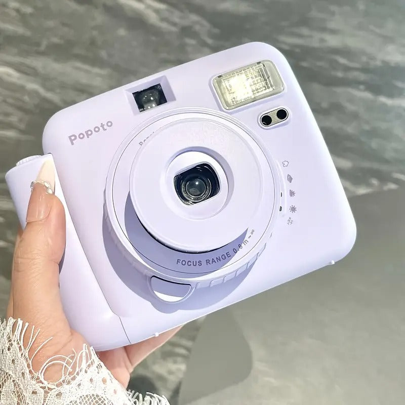 White Popoto instant camera held by a hand with a blurred natural background