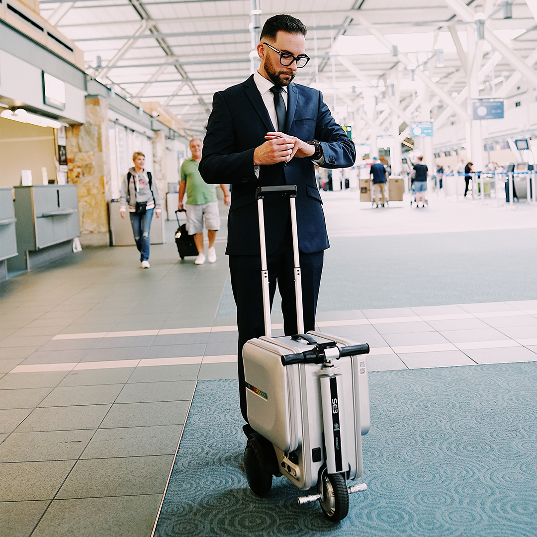 Man in a suit with a suitcase and scooter in an airport terminal