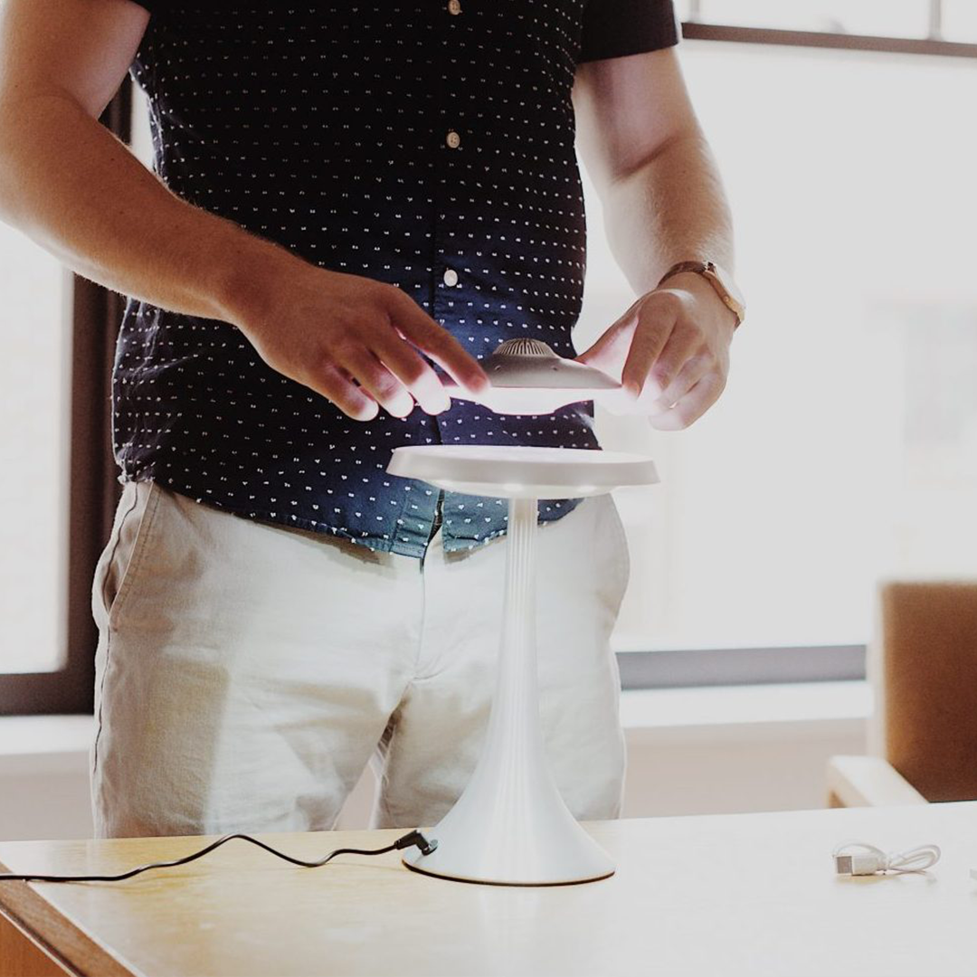 Person holding a white lampshade over a table with a blurred background